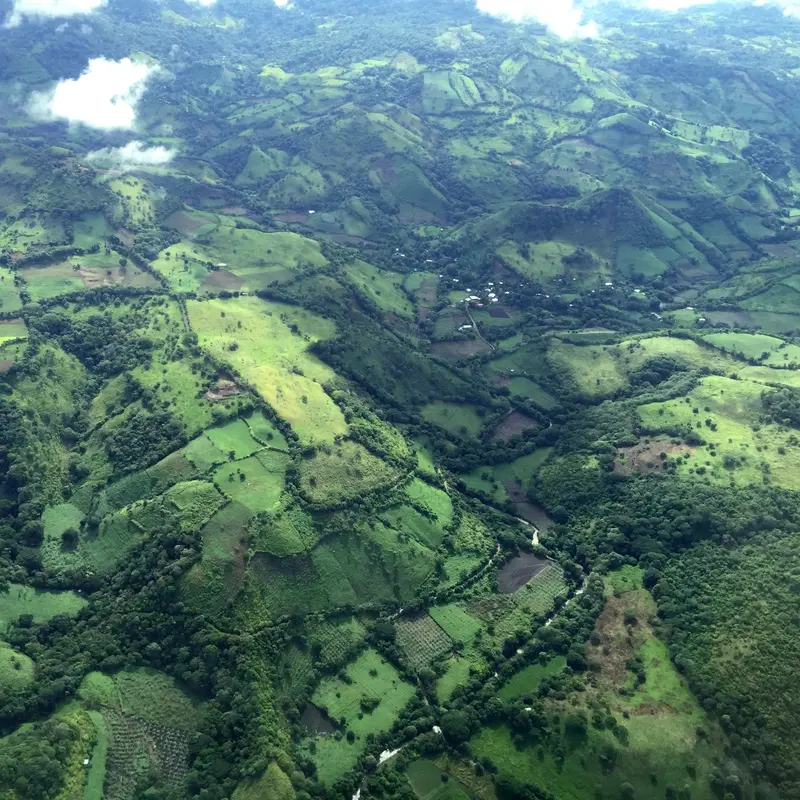 Drohnenaufnahme einer Landschaft mit Feldern, Wäldern und Hügeln. 