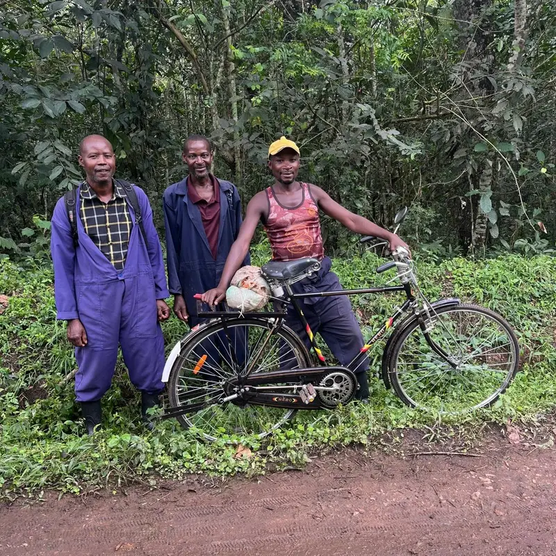Drei Personen stehen mit einem Fahrrad an einem Weg im Regenwald in Uganda. 