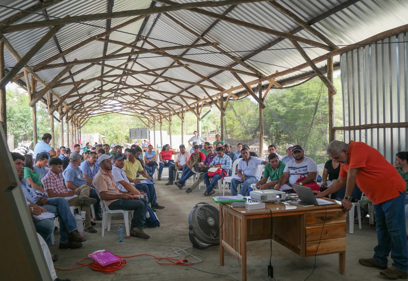 Gruppe von Personen sitzt unter einem Dach, ein Mann spricht.