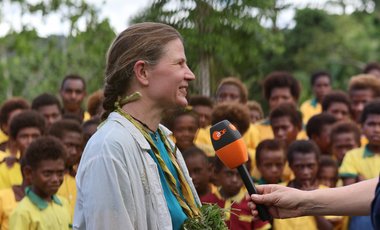 Eine Frau mit Naturschmuck spricht ins ZDF-Mikrofon, hinten eine Schulklasse. 